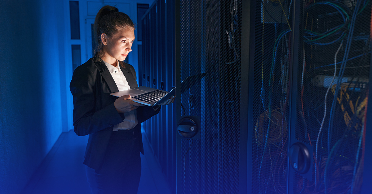 A woman in a business suit holding a laptop while inspecting servers in a data center.