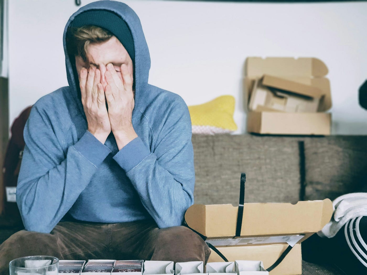 A person wearing a hoodie sits on a couch with their head in their hands.