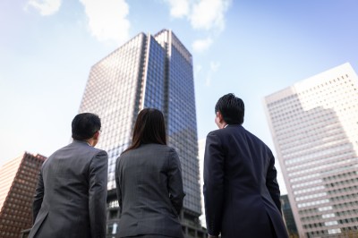 Three business professionals looking up at a modern skyscraper.