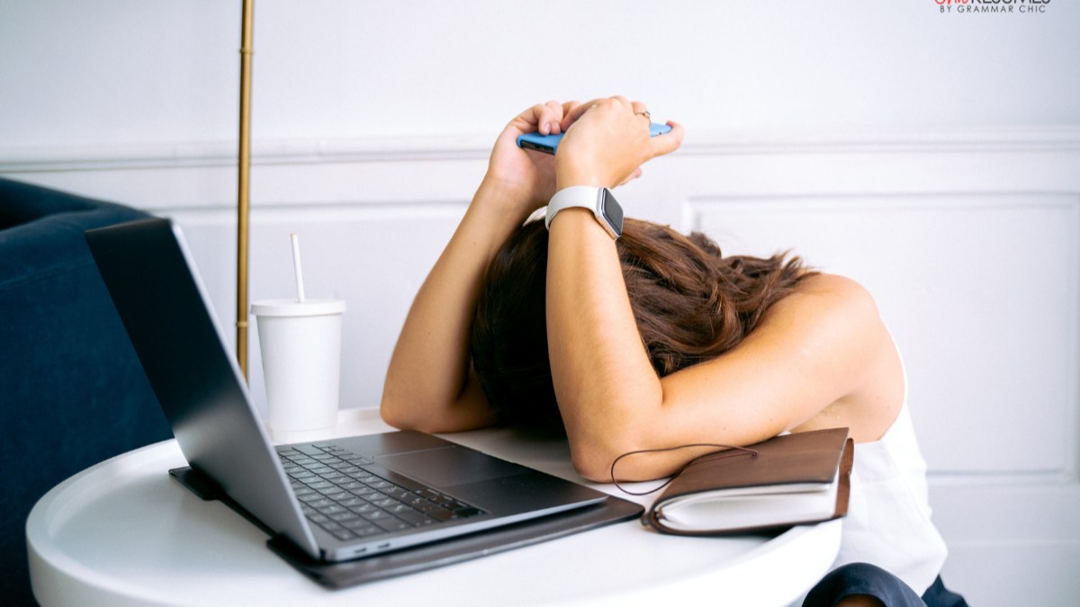 A frustrated person leaning their head down on their arms at a desk with a laptop.