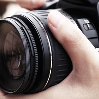 A close-up of a person's hand adjusting the focus on a large camera lens.