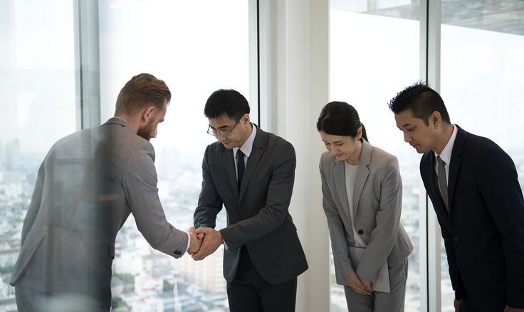 Japanese business people bowing respectfully during a handshake between colleagues.