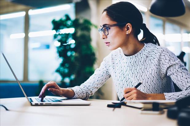 A focused woman with glasses working on a laptop in an office.