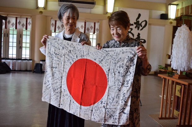 Two smiling elderly Japanese women holding up a returned Yosegaki Hinomaru flag.