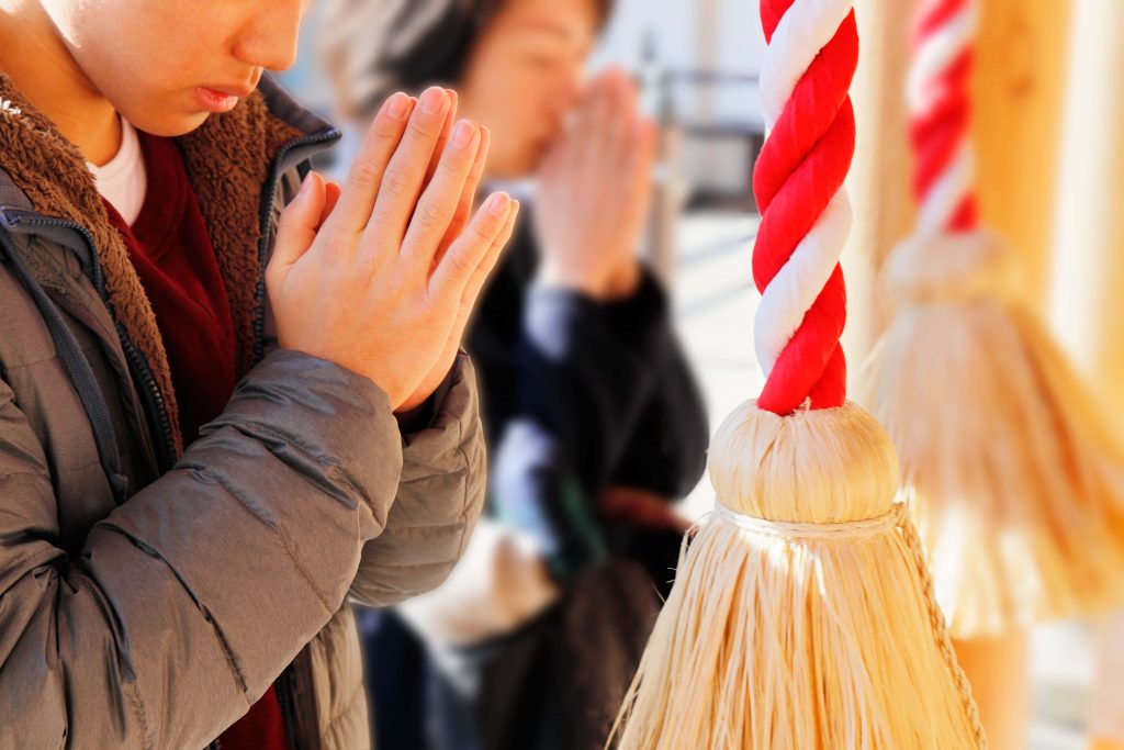 A person with hands pressed together in prayer at a Japanese shrine.