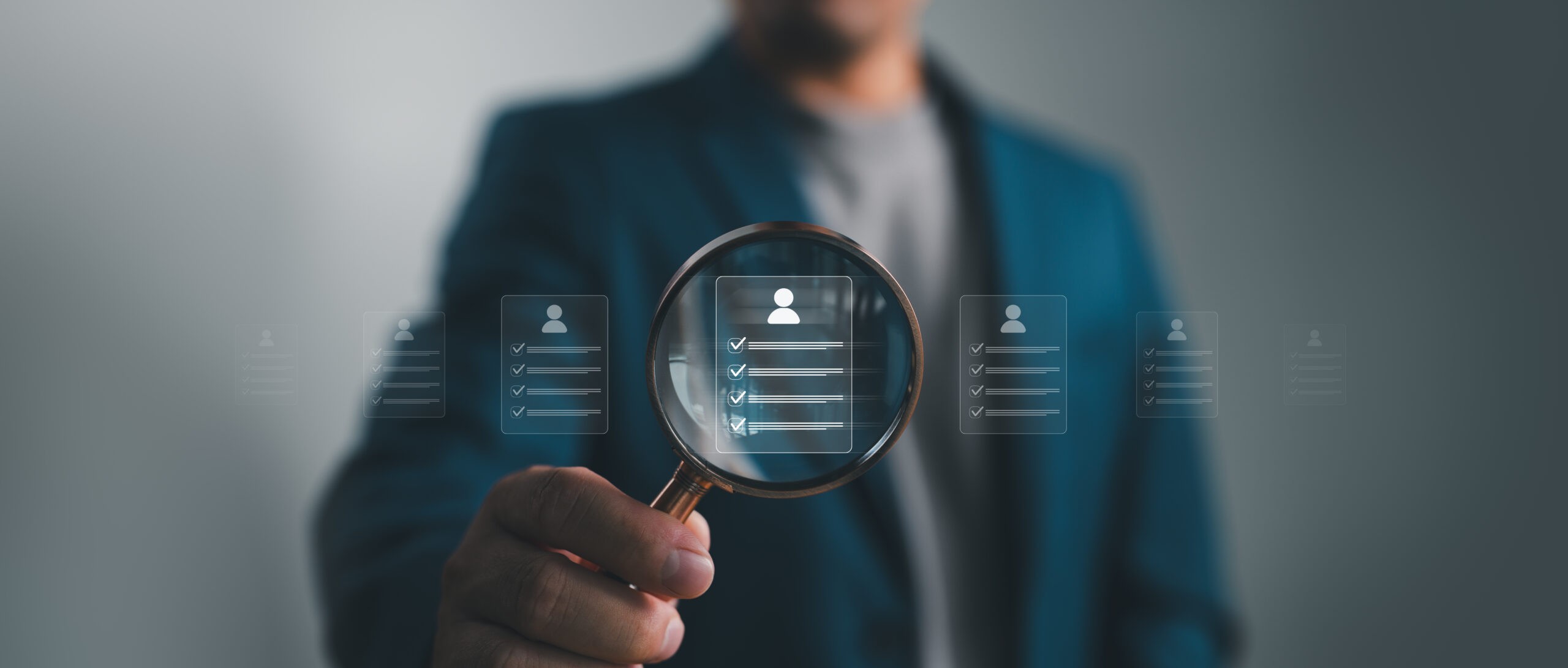 A person holding a magnifying glass over a digital representation of an employee profile with a checklist.