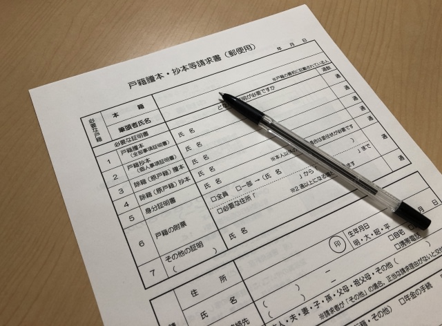 A Japanese official document (koseki) with a black pen resting on it.
