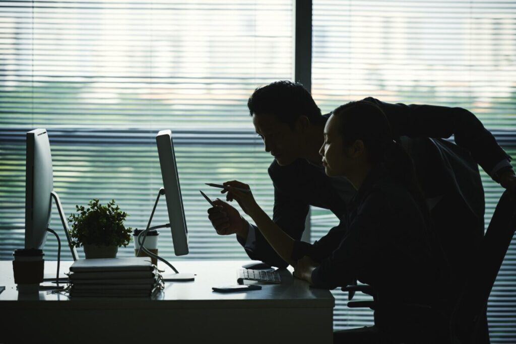 Silhouettes of two people working together at a computer in an office.