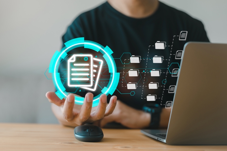 A person holding a glowing digital icon representing documents, with a laptop in the background.