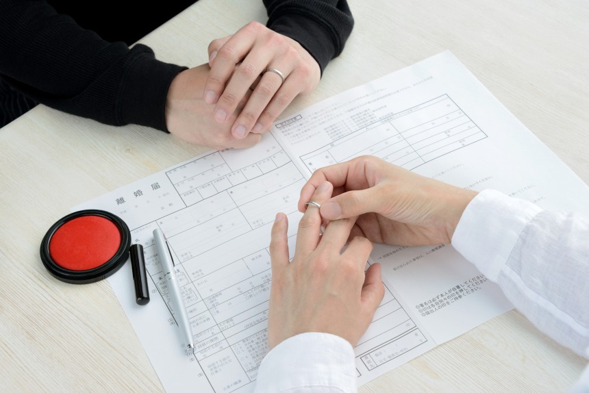 Hands signing a Japanese divorce document with a traditional hanko stamp nearby.