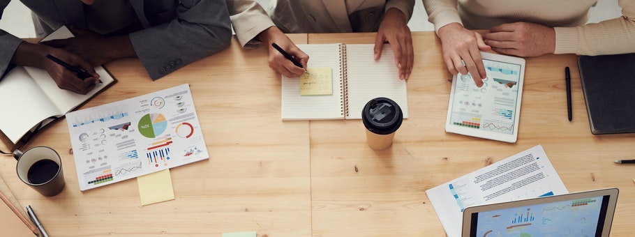 An overhead view of a business meeting with people reviewing charts and using a tablet.