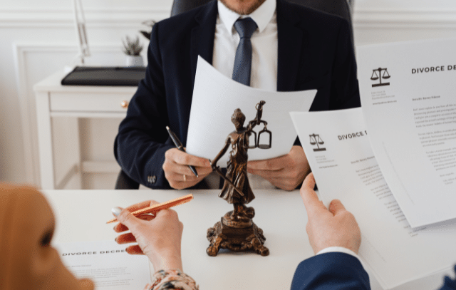 A lawyer reviewing divorce papers with clients, with a statue of Lady Justice on the desk.