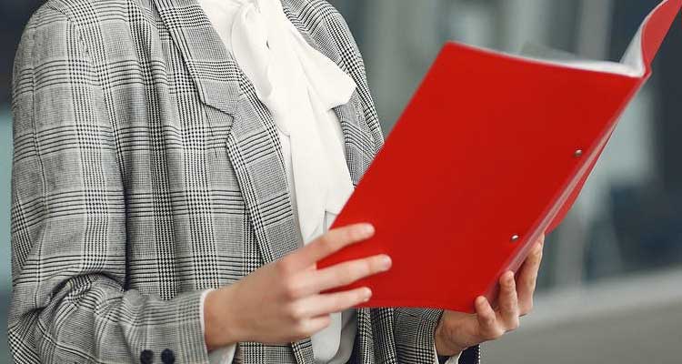 A person in a business suit holding an open red binder.