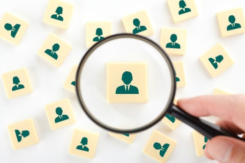 A magnifying glass hovering over a grid of person icons, focusing on one.