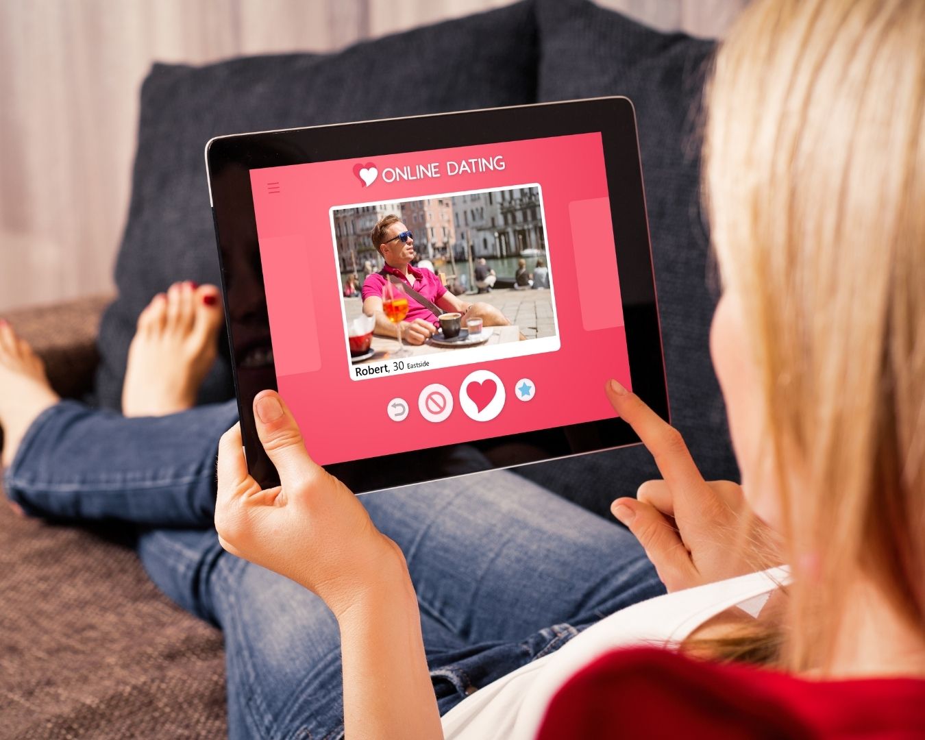Woman relaxing on a couch while browsing an online dating profile on a tablet.