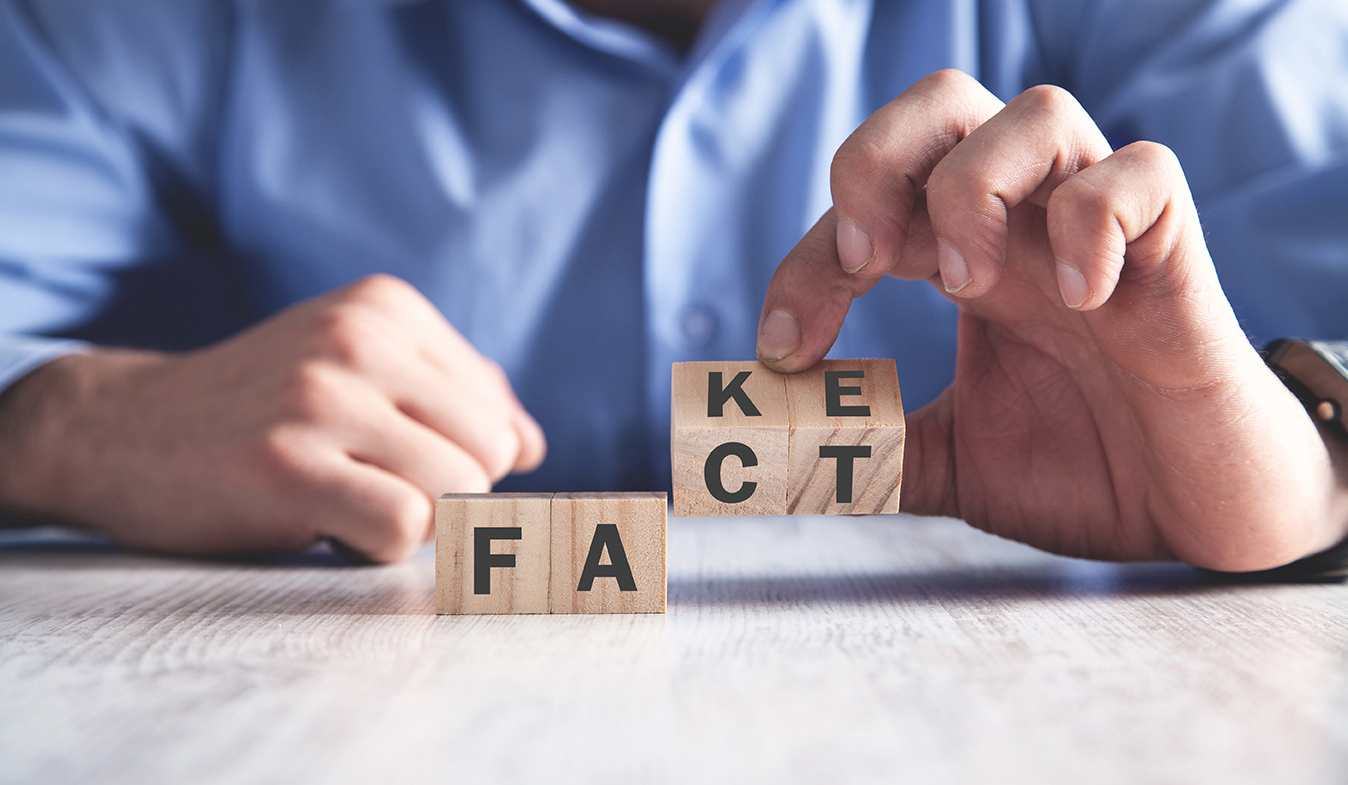 Hands arranging wooden blocks spelling FACT and FAKE.