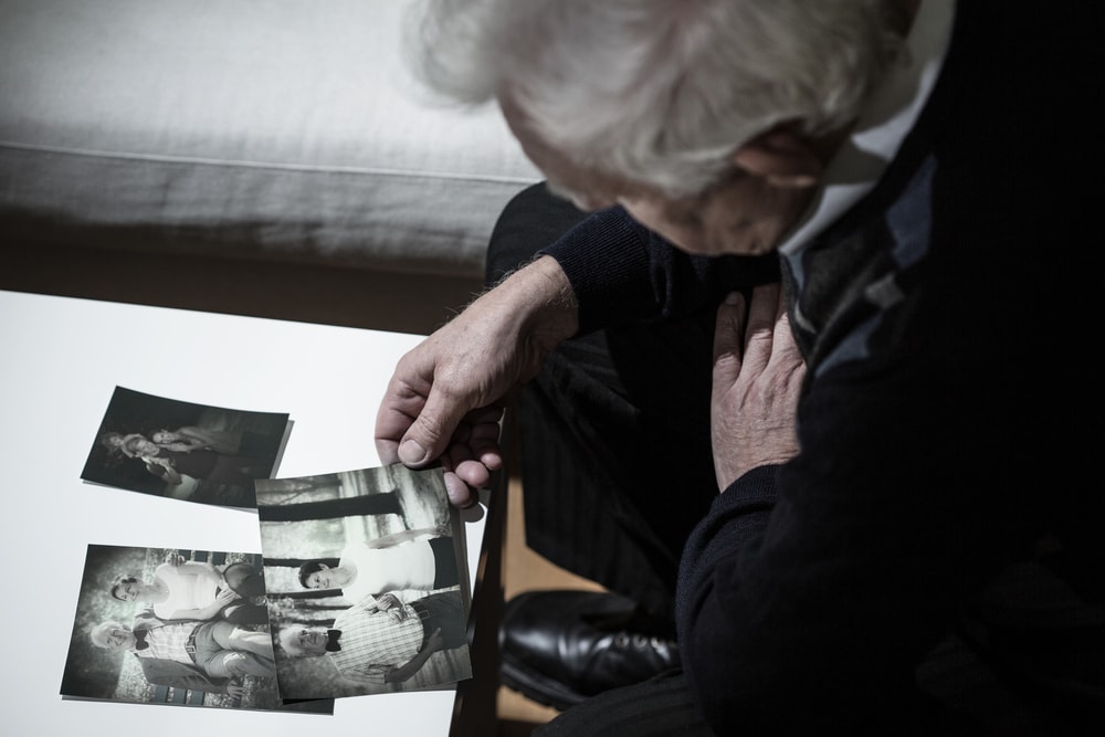 An elderly person looking down at a collection of old black and white family photographs.