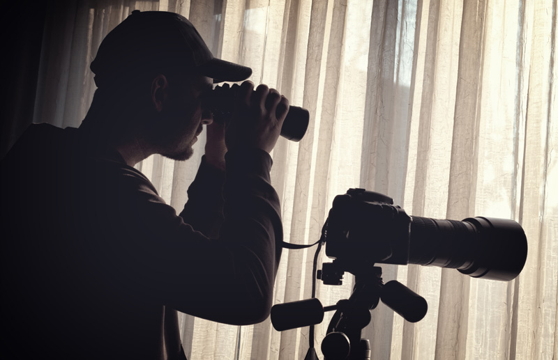 Silhouette of an investigator looking through binoculars with a camera on a tripod nearby.