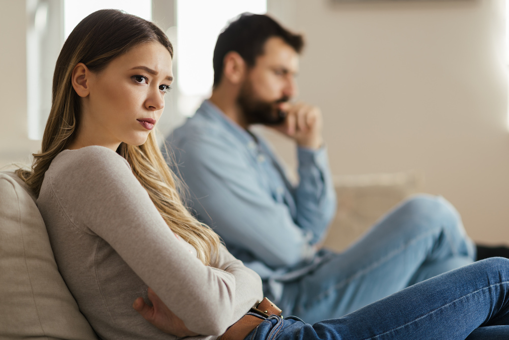 An unhappy couple sitting on opposite ends of a couch, facing away from each other.
