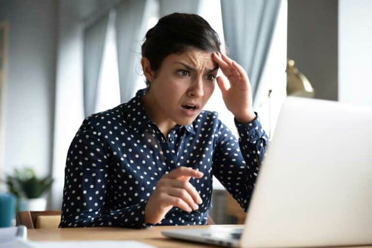 A woman looks at her laptop with a shocked and worried expression.