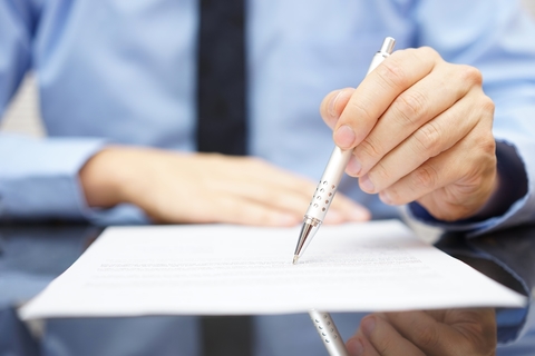 A close-up of a businessman's hand signing a legal document with a pen.