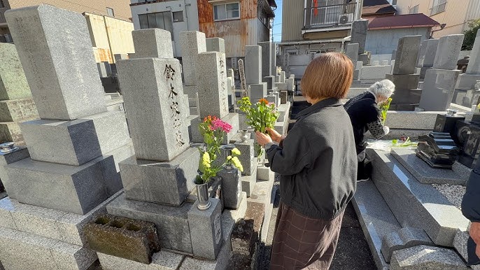 A woman placing flowers at a grave in a modern Japanese cemetery.
