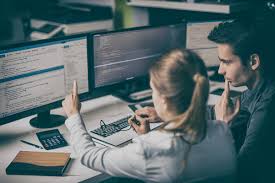Two investigators working together in front of multiple computer monitors with data.