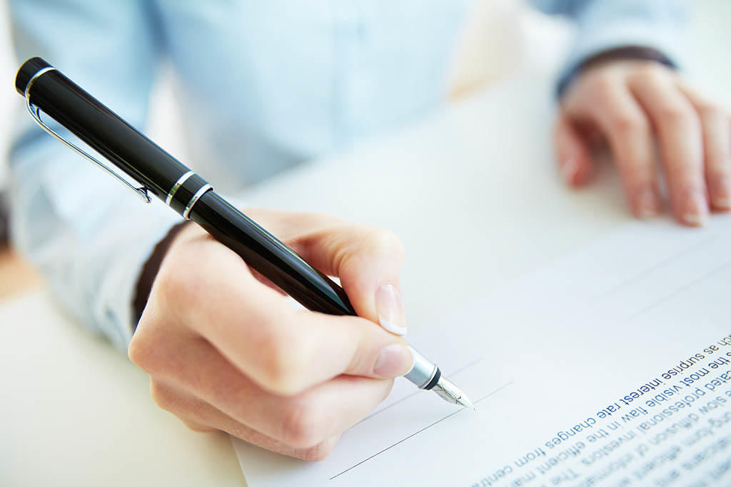A close-up of a hand writing on a form with a black pen.