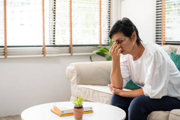 A frustrated woman sitting on a couch, pinching the bridge of her nose in stress.