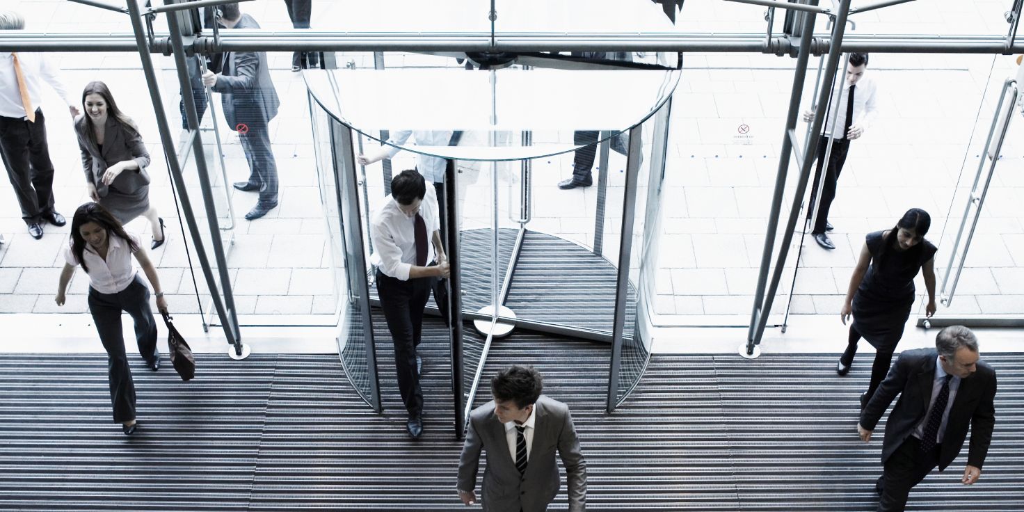Business people in suits walking through a revolving door at a modern office building.