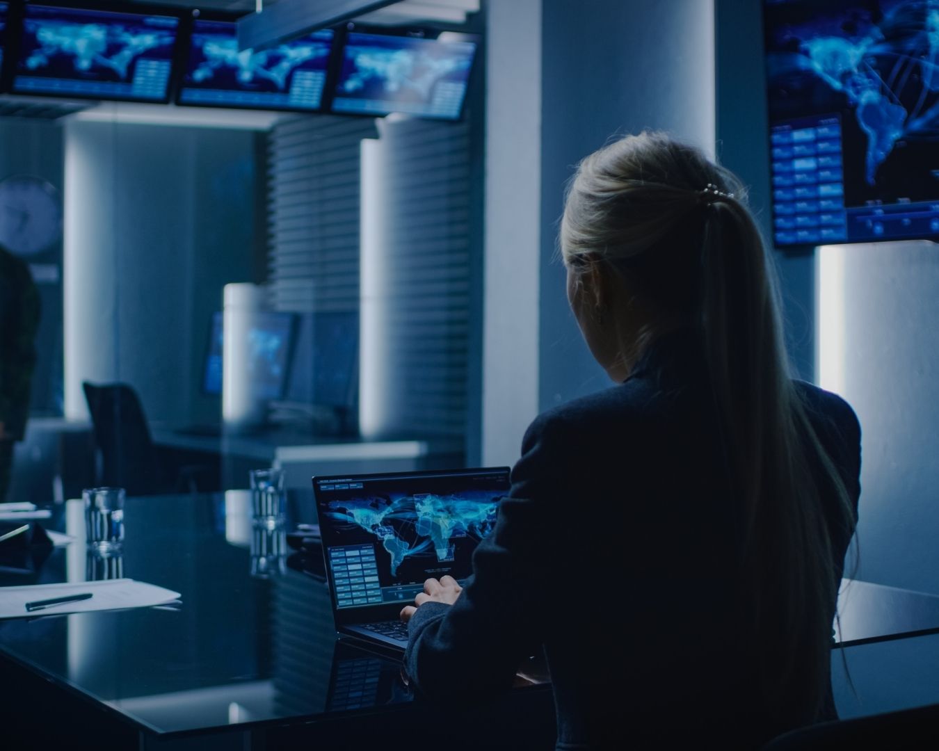 Investigator in a high-tech control room with multiple screens showing world maps.