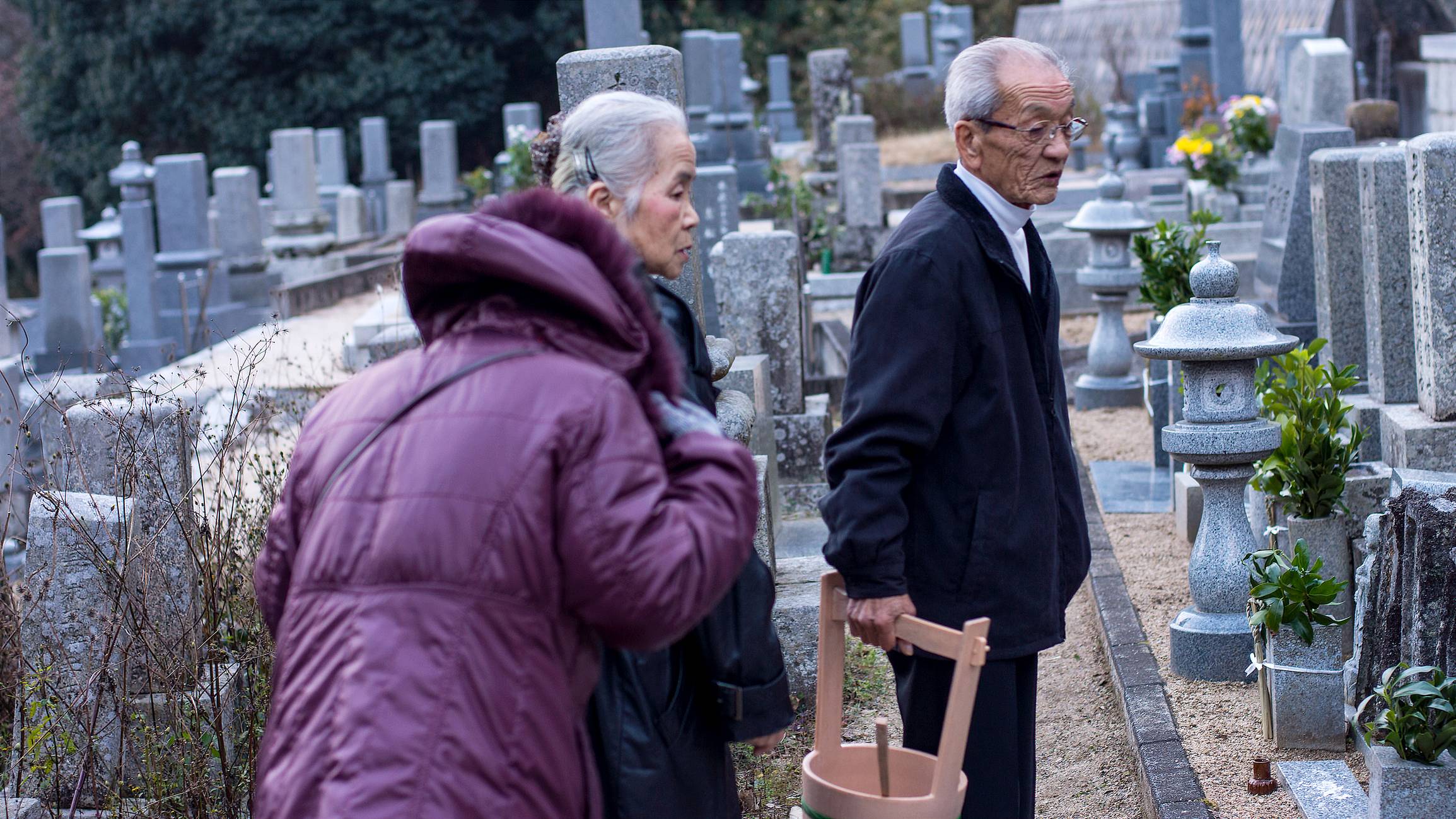 Three elderly people walking through a traditional Japanese cemetery.