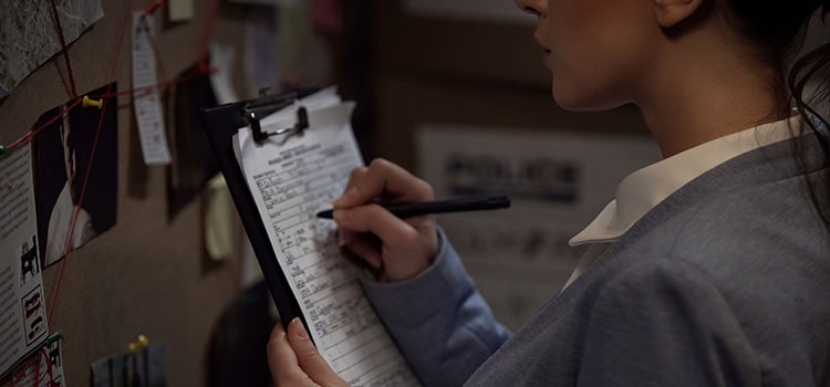 A close-up of an investigator writing notes on a clipboard.