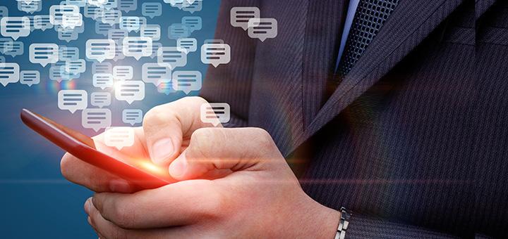 A person in a suit writing with a pen, with digital chat bubble icons floating around.