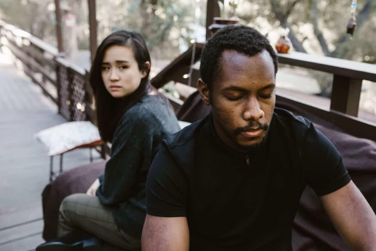 An unhappy couple sitting apart from each other on an outdoor deck.