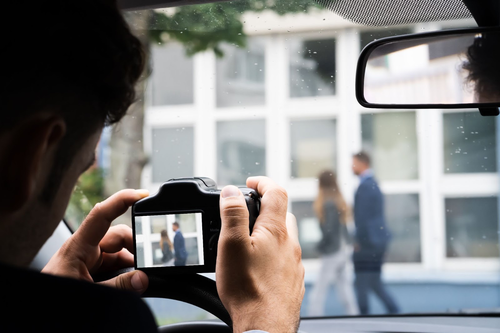 Investigator from inside a car, taking a surveillance photo of people walking on the street.