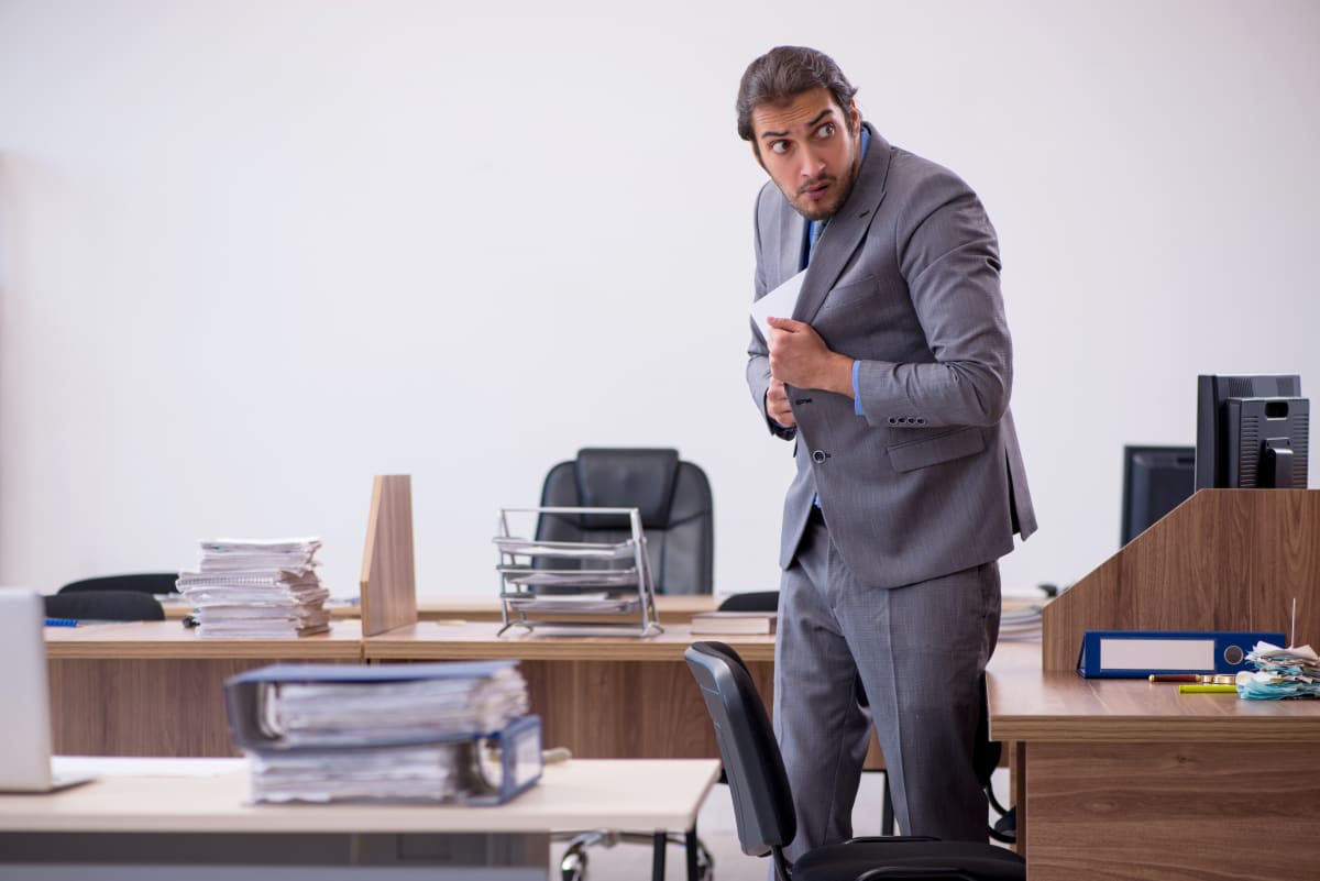 A man in a suit looks over his shoulder suspiciously while hiding a document in his jacket.