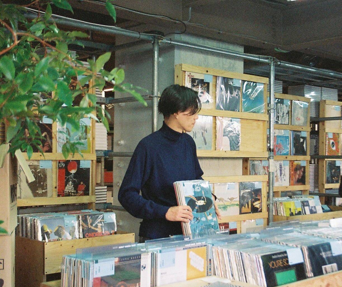 A person with short hair holding a vinyl record and browsing in a record store.