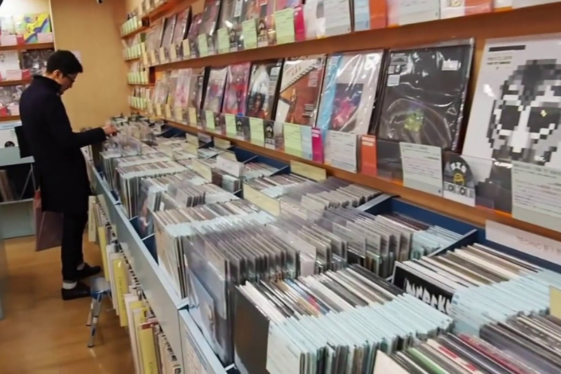 A man in a black coat browsing through vinyl records in a well-lit store.