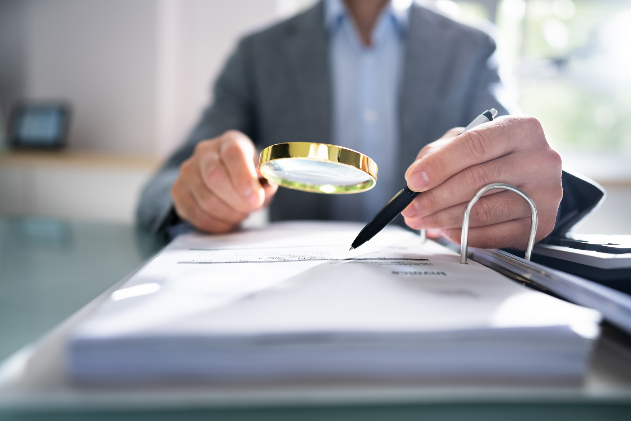 A person using a magnifying glass to examine a document on a desk.